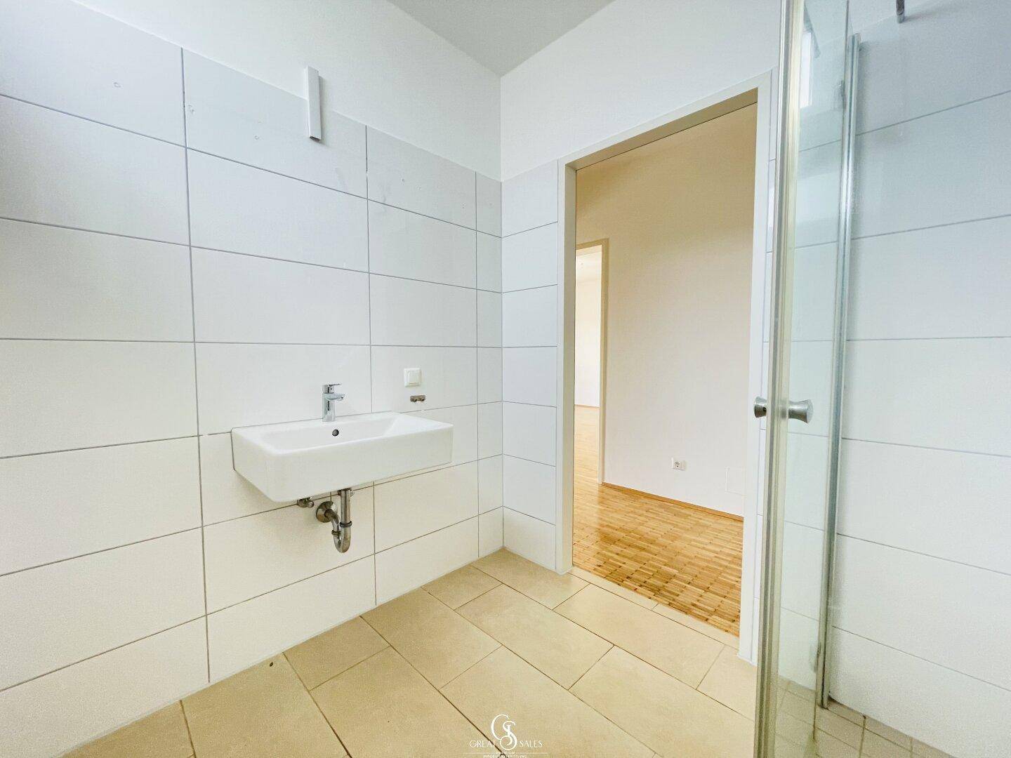 Modernes Badezimmer mit weißen Fliesen, wandhängendem Waschbecken und Duschkabine.