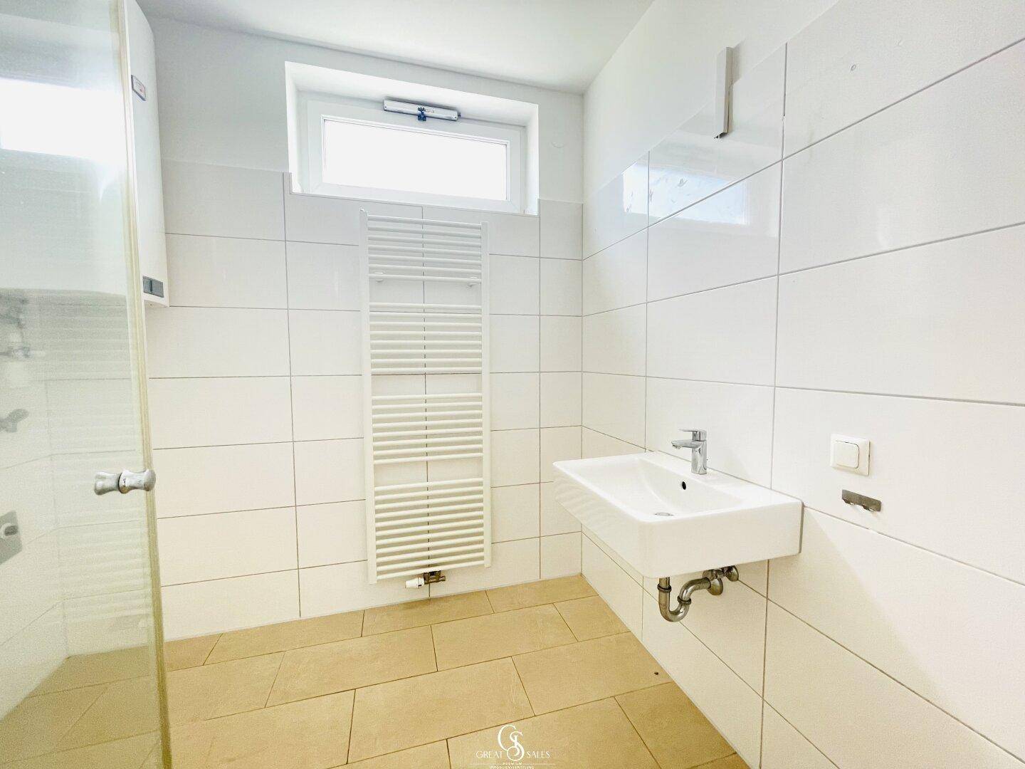 Badezimmer mit Fenster, wandhängendem Waschbecken und praktischem Handtuchheizkörper.