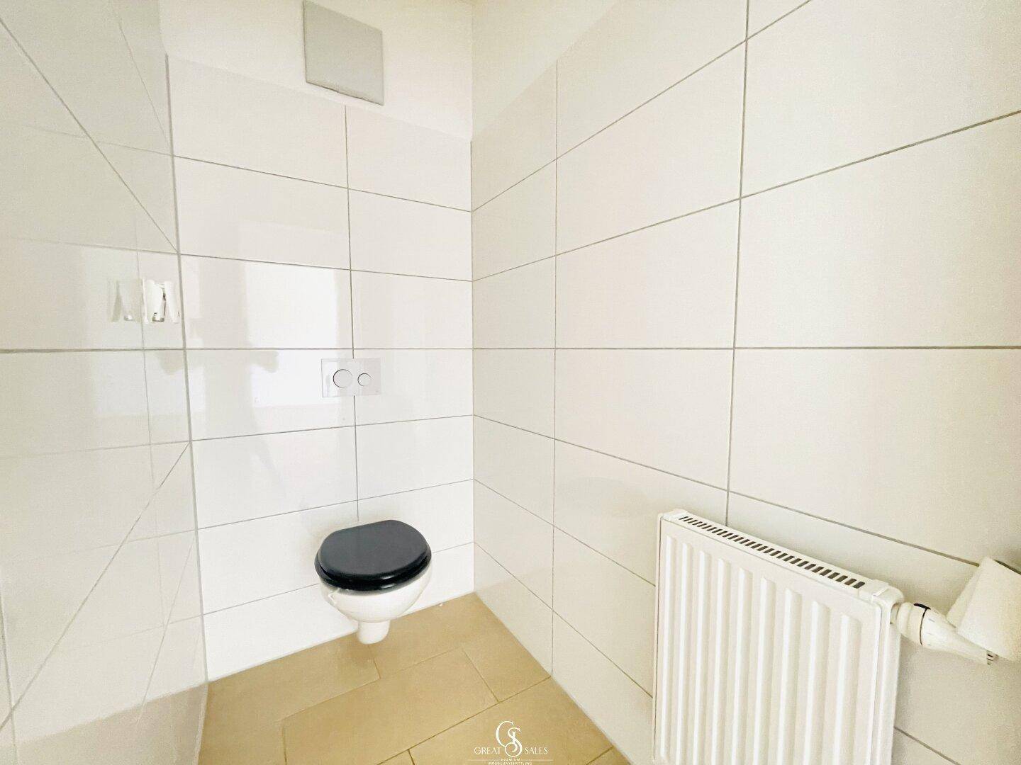 Separates WC mit wandhängender Toilette, weißen Fliesen und Heizkörper.