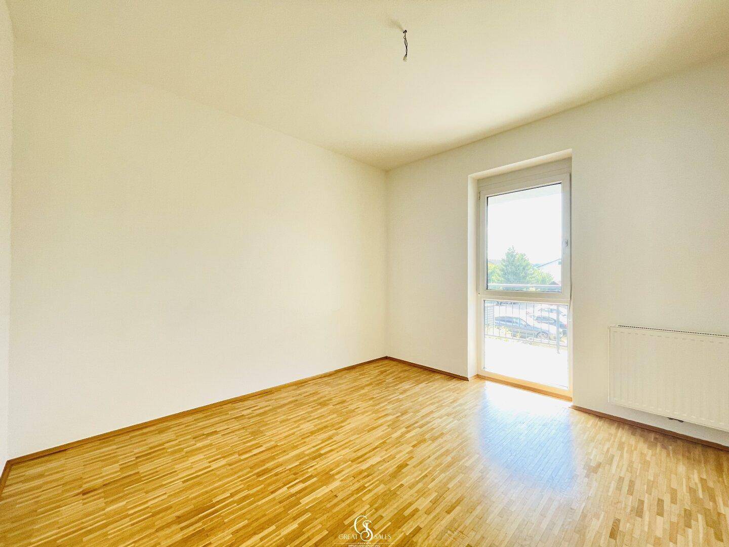 Helles Zimmer mit Parkettboden und großem Fenster, ideal als Schlaf- oder Arbeitszimmer.