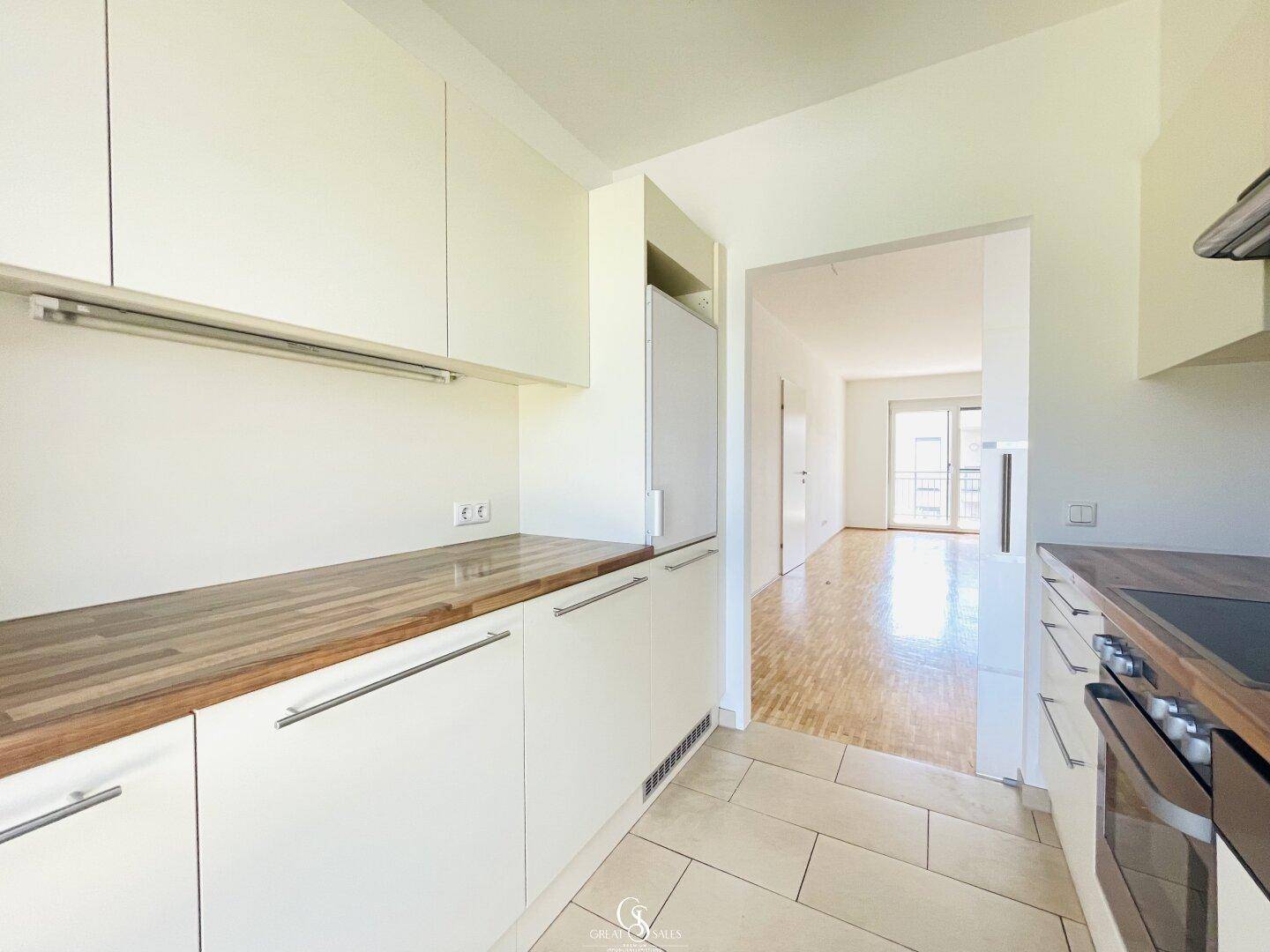 Moderne Küche mit hellen Schränken, integriertem Kühlschrank und offenem Zugang zum Wohnbereich.