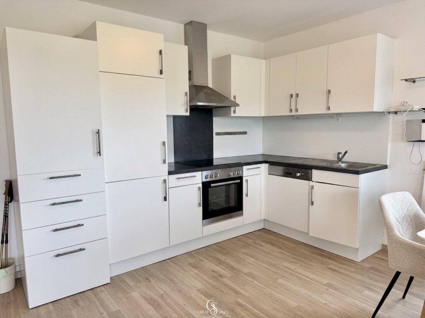 Moderne weiße Einbauküche mit schwarzen Arbeitsplatten, integrierten Geräten und Dunstabzugshaube.