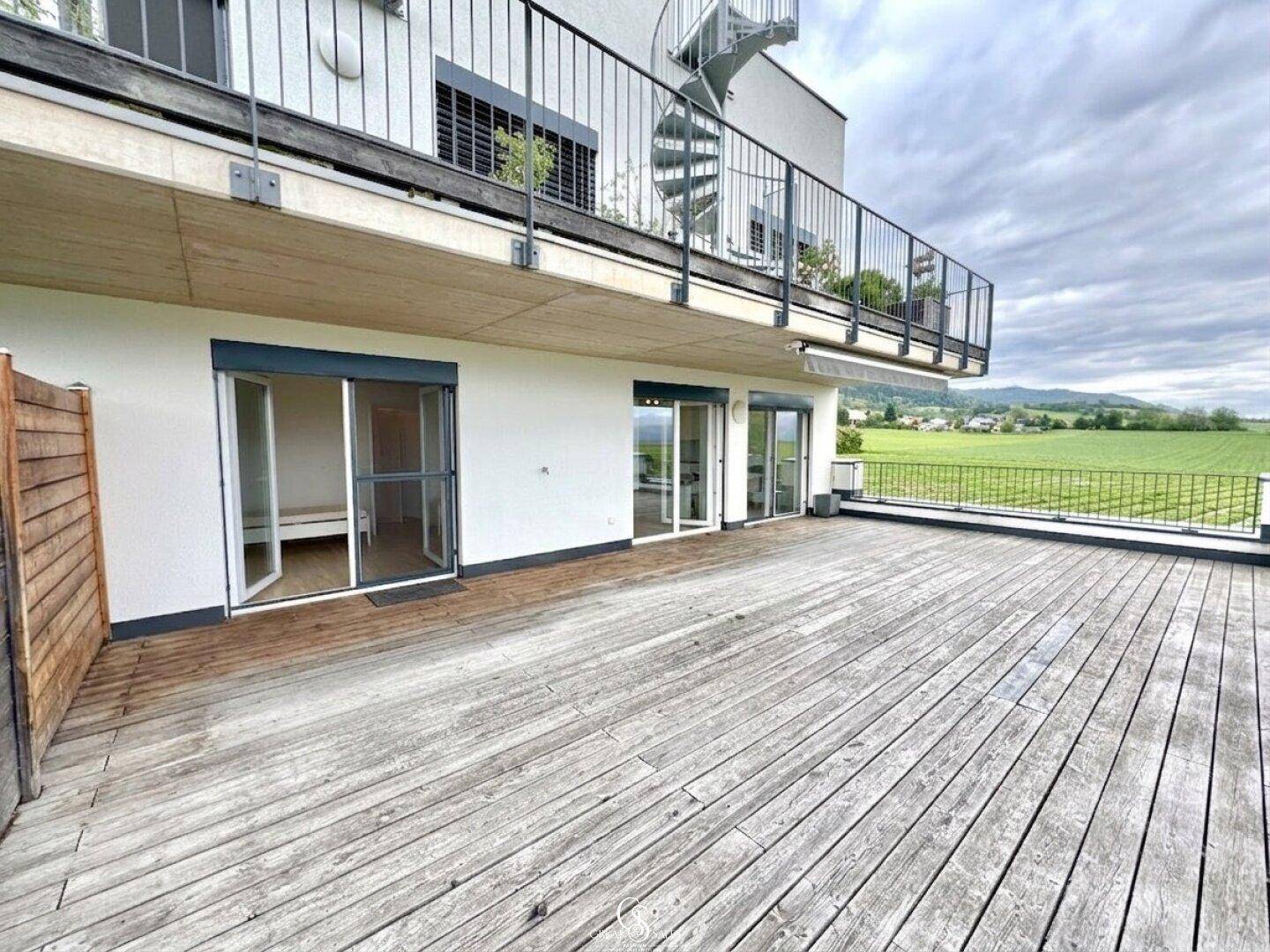 Große Holzterrasse mit Schiebetüren zum Innenbereich und Blick auf die umliegende Landschaft.