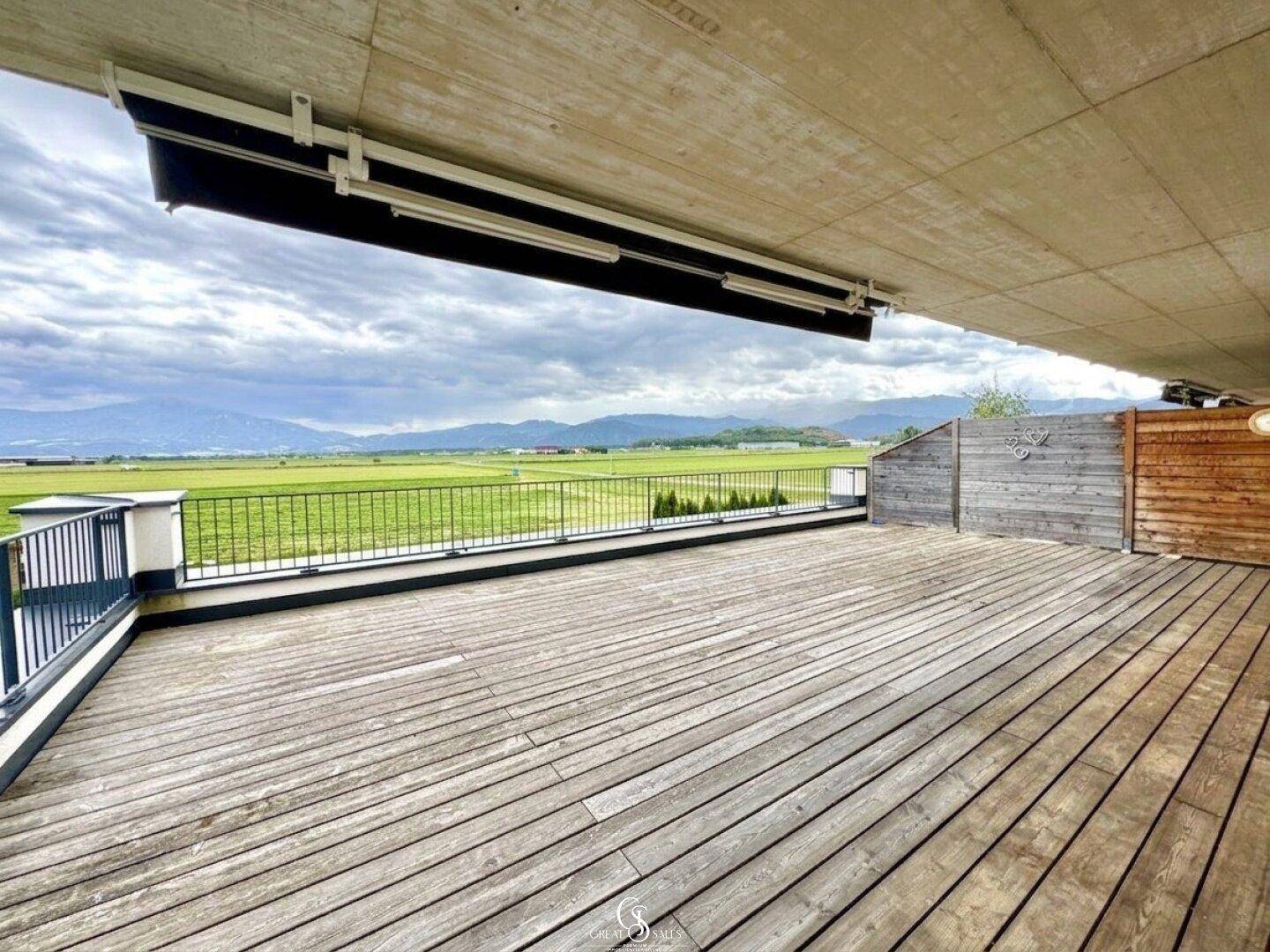 Weitläufige Holzterrasse mit Blick auf die grüne Landschaft und die entfernten Berge.