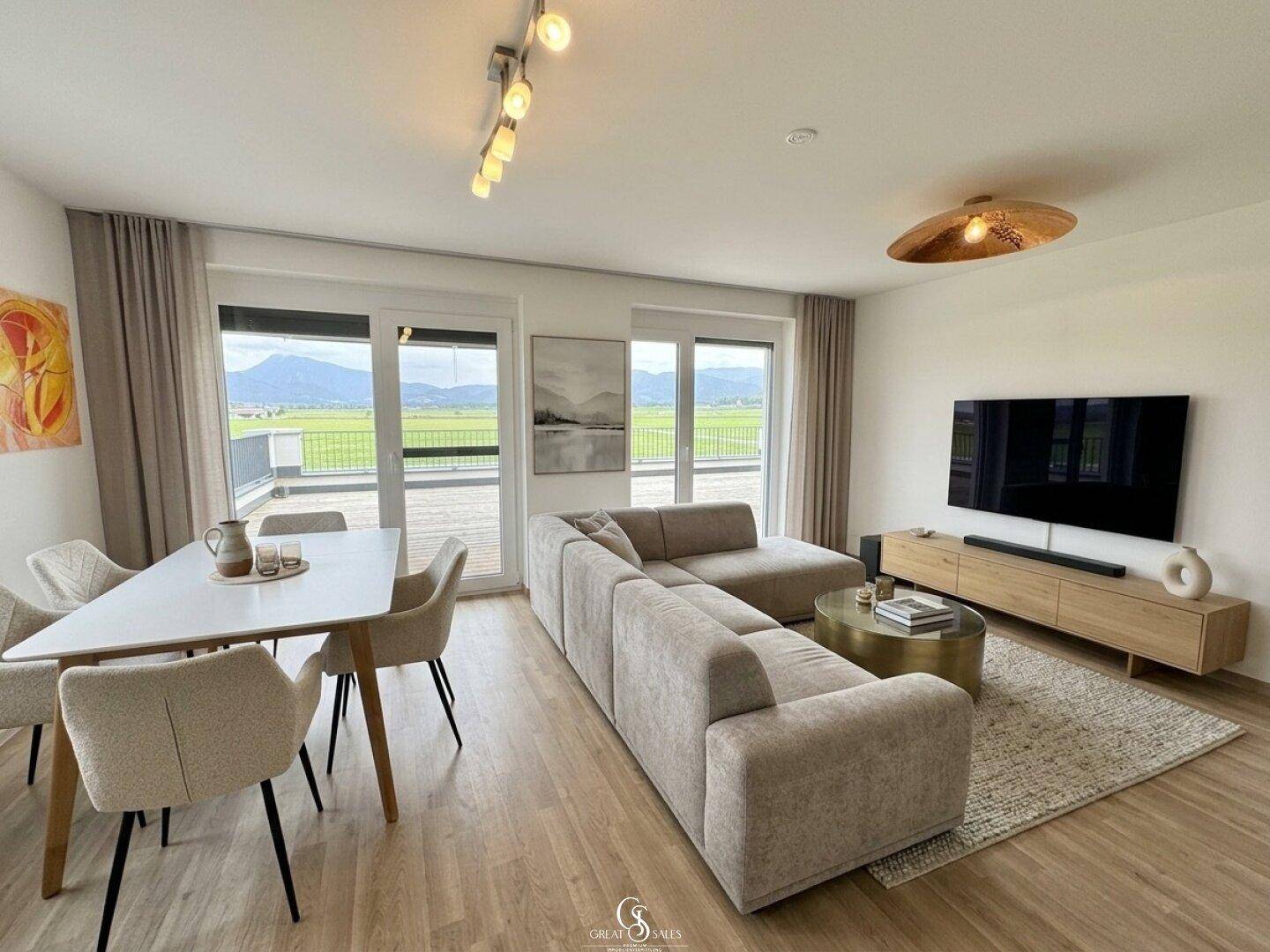 Heller Wohn-Essbereich mit modernem Sofa, Esstisch und Zugang zur Terrasse mit Bergblick.