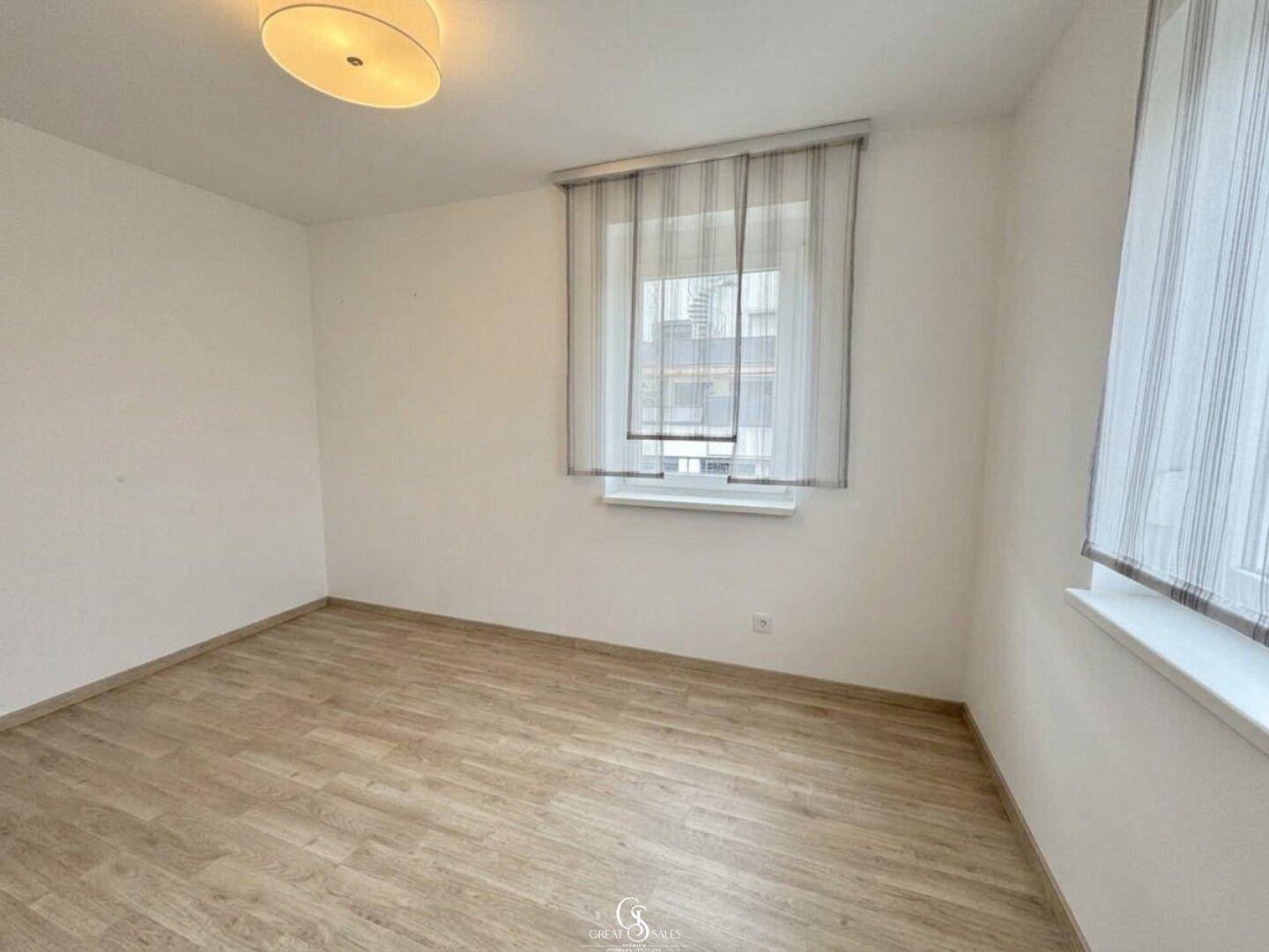 Leeres Zimmer mit hellem Laminatboden und einem Fenster, ideal als Schlaf- oder Arbeitszimmer.