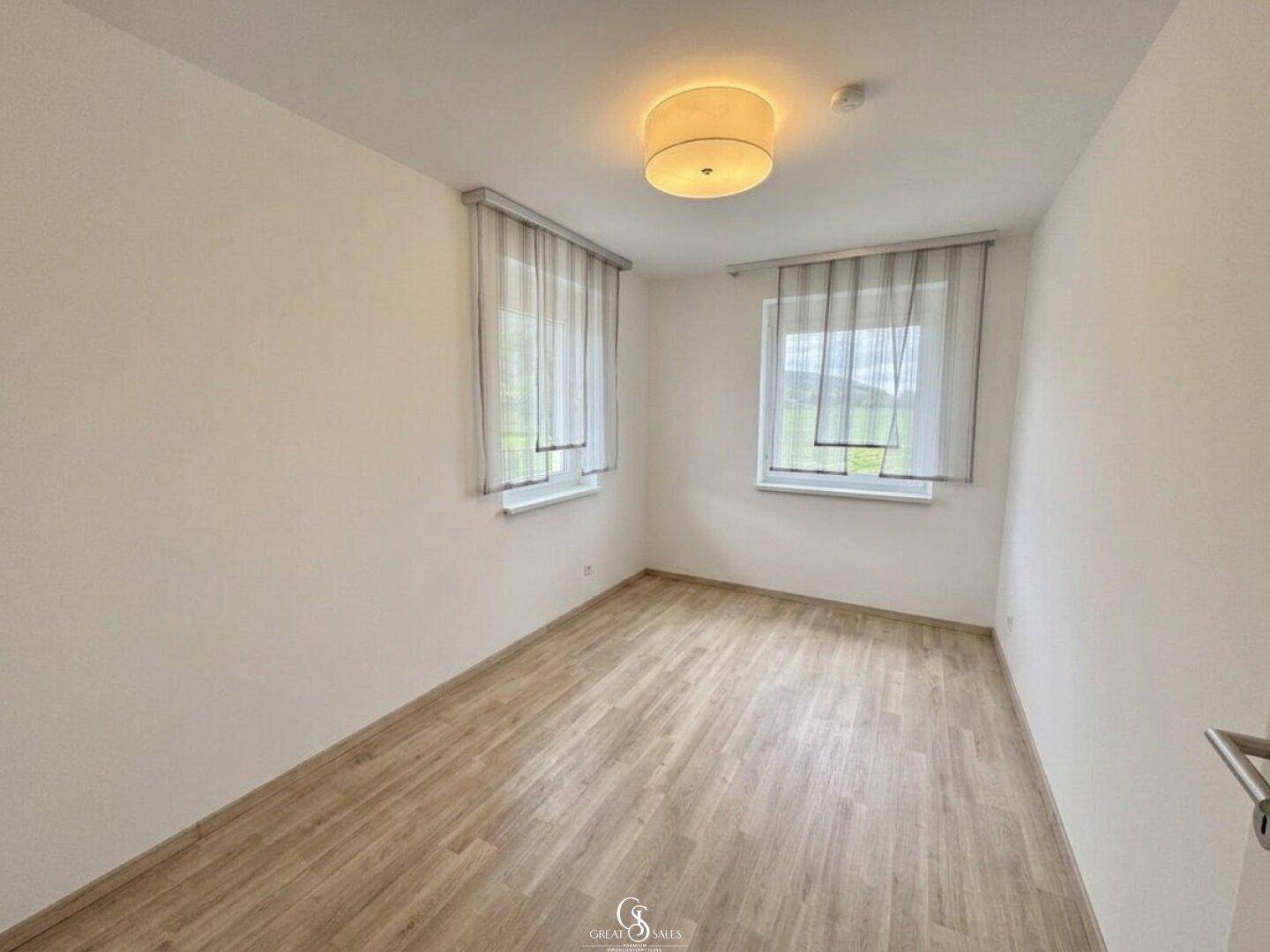 Helles, leeres Zimmer mit Laminatboden und zwei Fenstern, vielseitig nutzbar.
