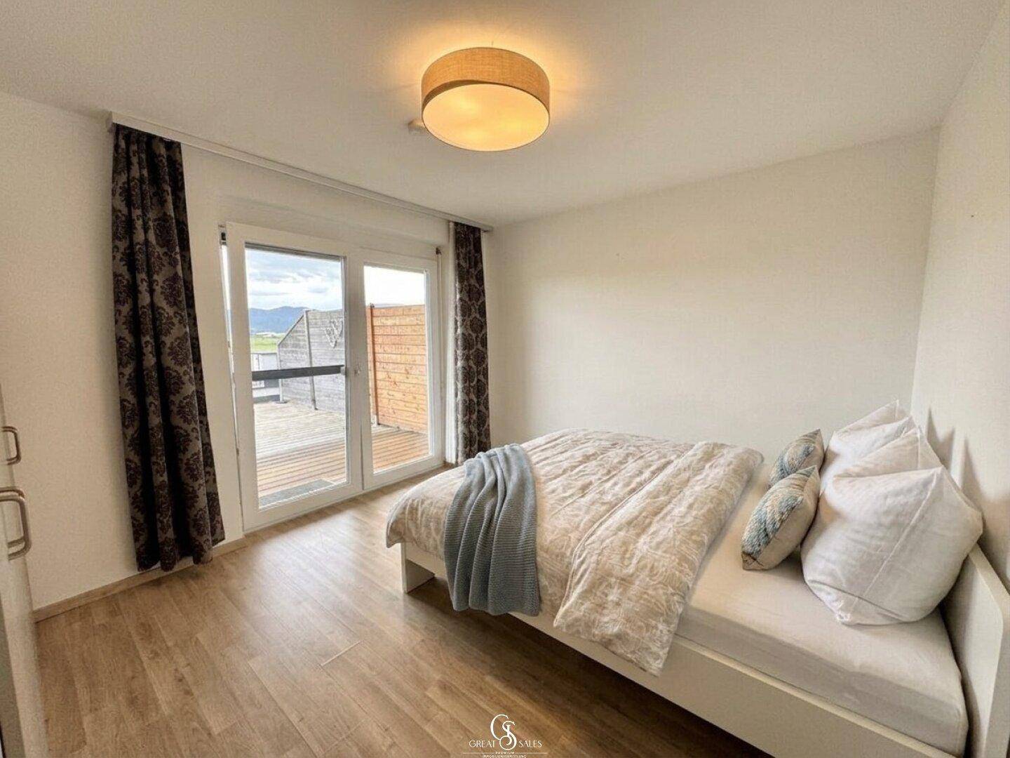 Schlafzimmer mit hellem Laminatboden, Bett und direktem Zugang zu einem Außenbereich.