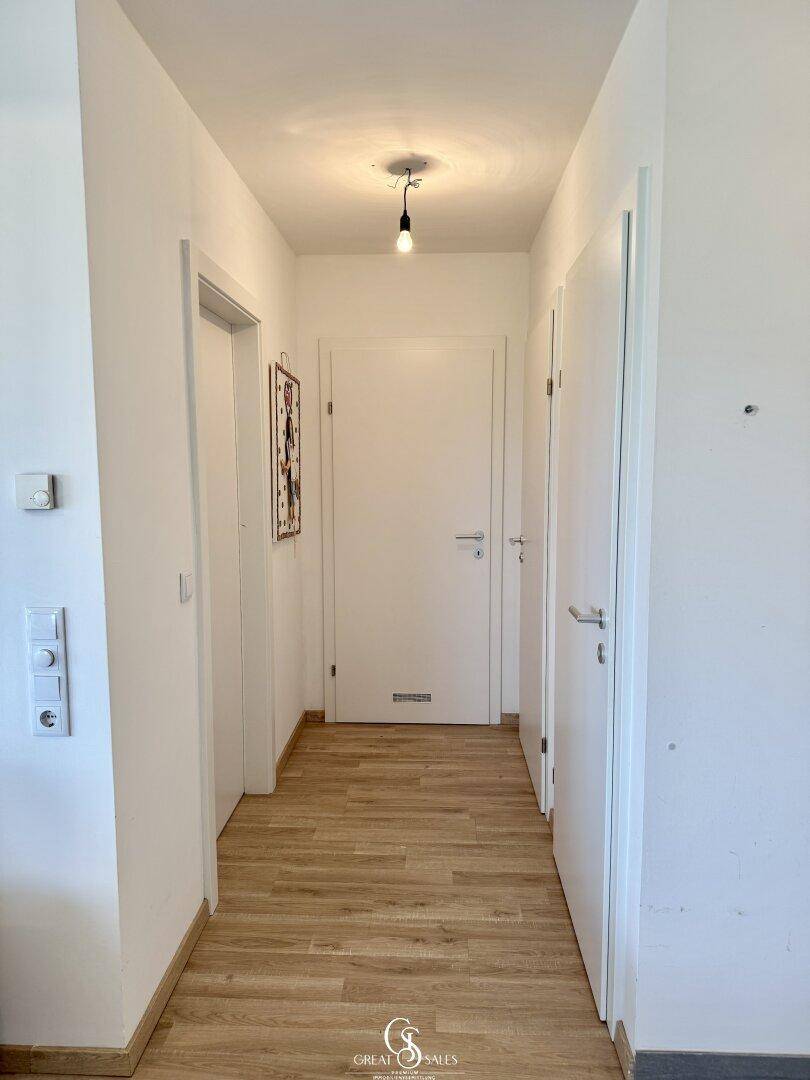 Schmaler Flur mit hellem Laminatboden und mehreren weißen Türen zu den angrenzenden Räumen.