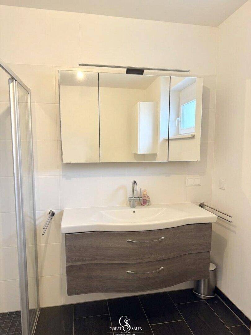 Detailansicht des Badezimmers mit modernem Waschtisch, großem Spiegelschrank und Fenster.