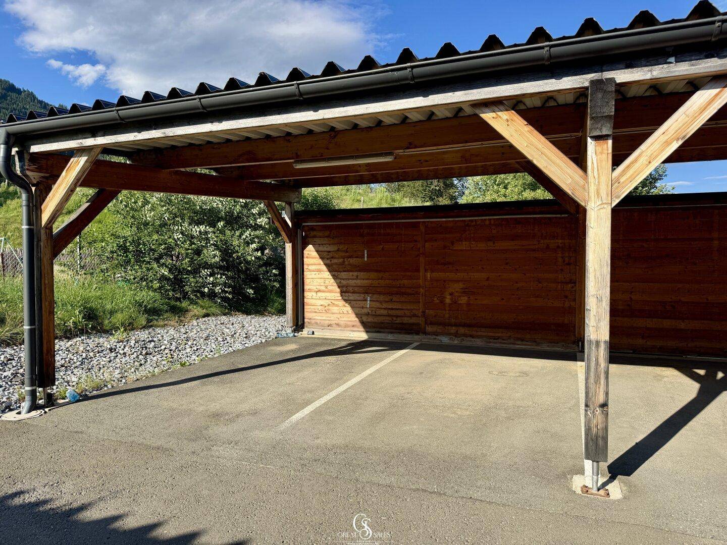 Geräumiger Holz-Carport mit asphaltiertem Stellplatz, bietet Schutz für Fahrzeuge.