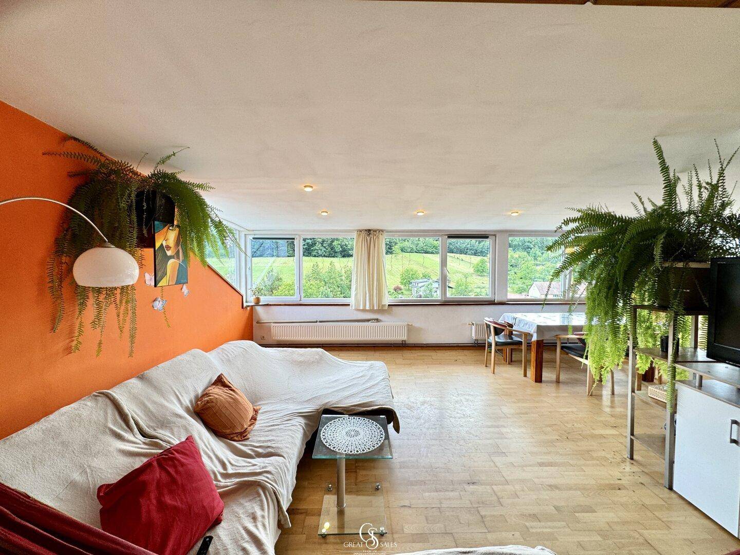 Helles Wohn- und Esszimmer mit Holzboden, großen Fenstern und Blick ins Grüne.