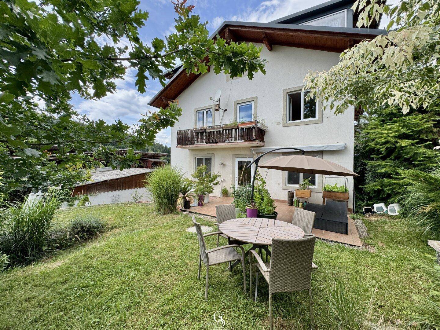 Gartenbereich mit Sitzgelegenheiten und Blick auf das Wohnhaus mit Balkon.