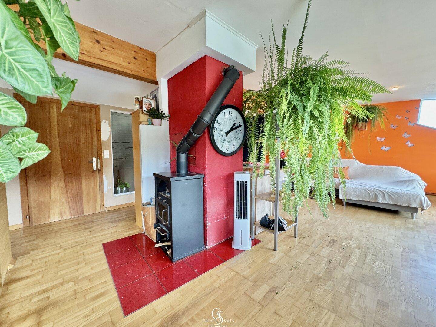 Wohnbereich mit einem modernen Holzofen, roter Wand und Holzboden.