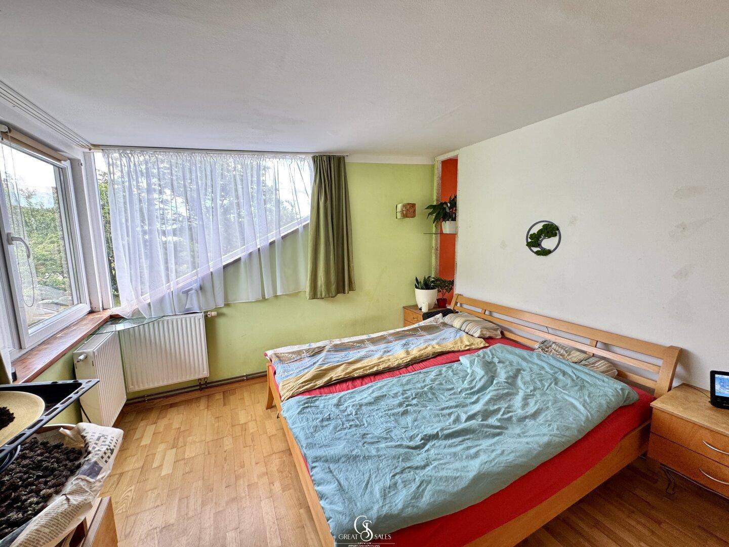 Schlafzimmer mit Holzbett, grünen Wänden und großen Fenstern mit Ausblick.
