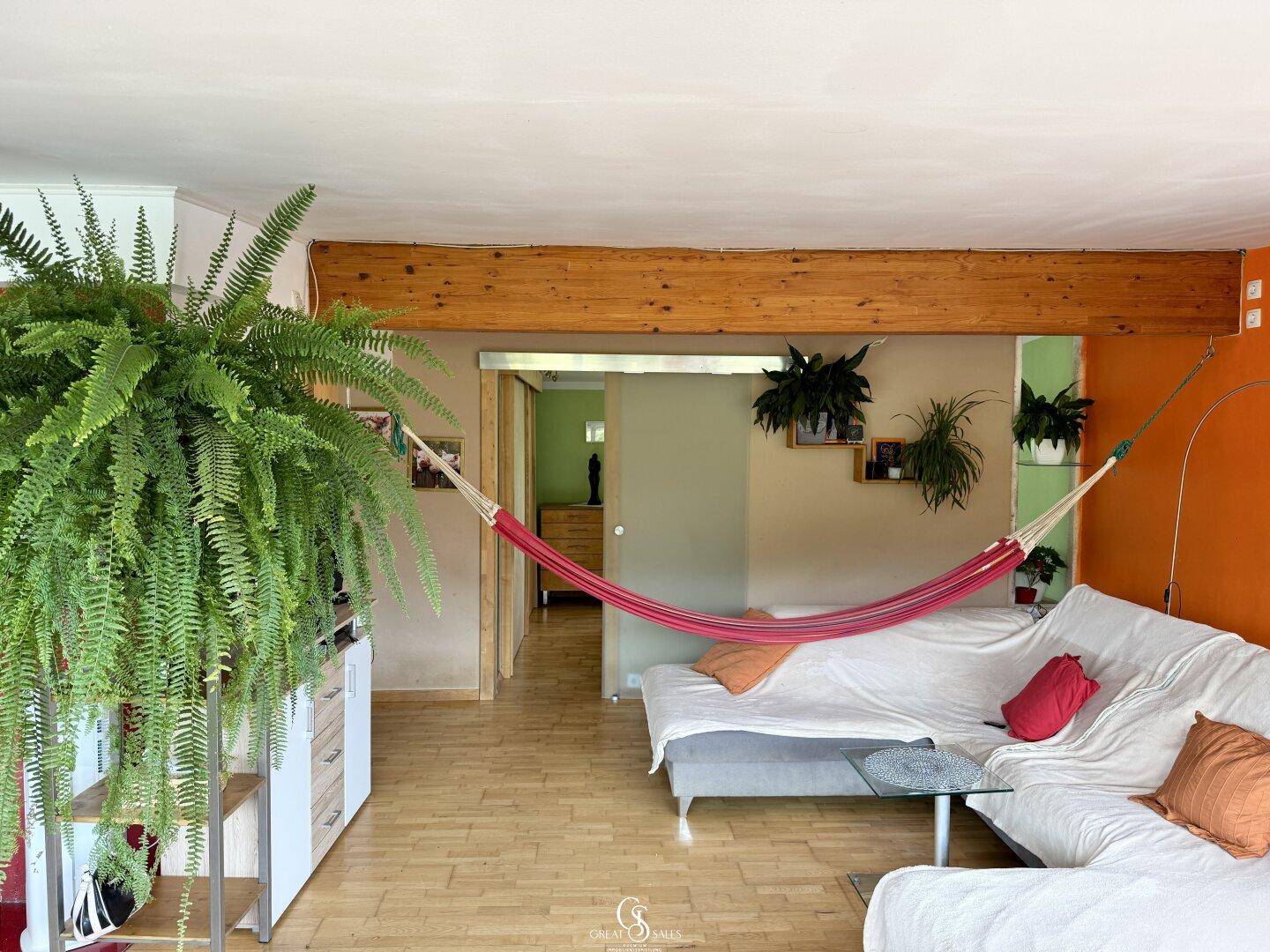 Gemütlicher Wohnbereich mit Hängematte, Sofa und Holzbalken an der Decke.