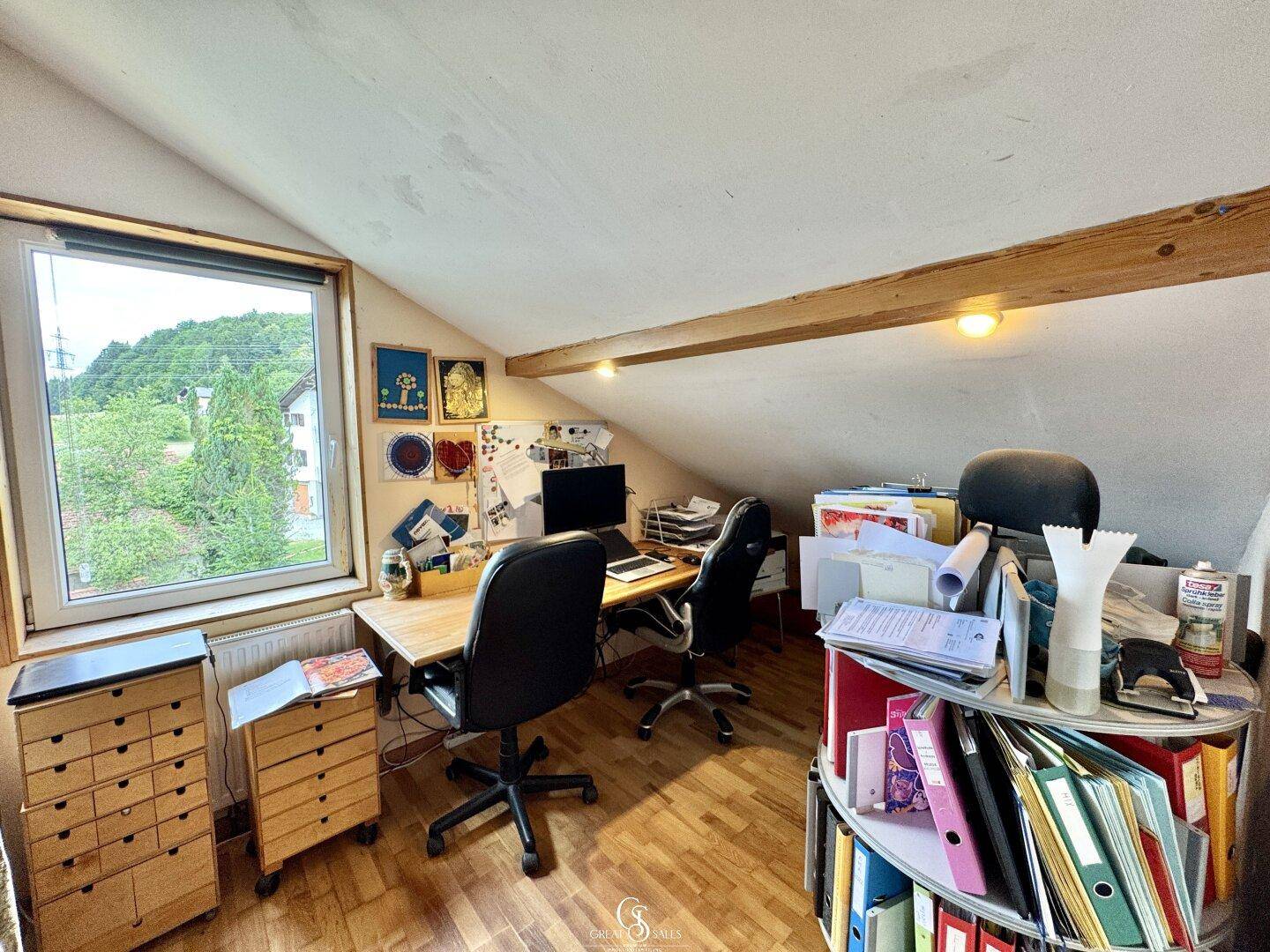 Dachgeschossbüro mit Holzbalken, Schreibtischen und Blick ins Grüne.