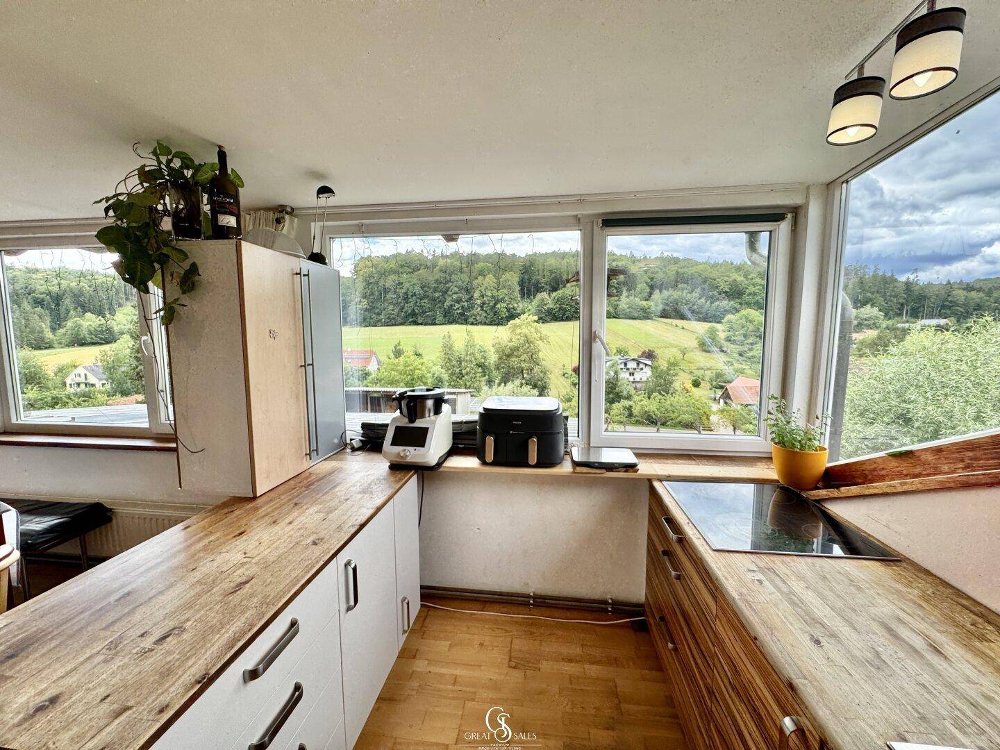 Helle Küche mit Holzarbeitsplatten, Induktionskochfeld und weitem Blick ins Grüne.