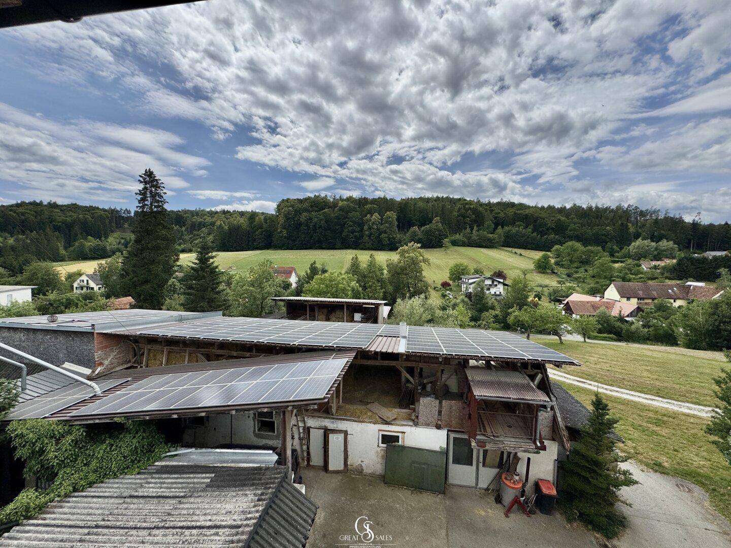 Weitläufiger Blick auf landwirtschaftliche Gebäude mit Solaranlagen und umliegender Natur.