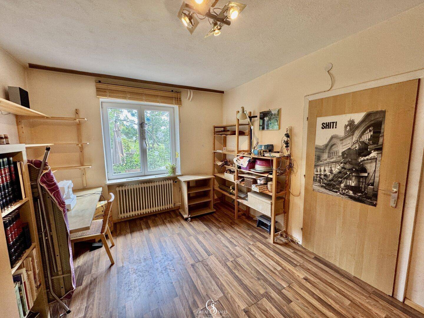 Helles Zimmer mit Holzfußboden, Fenster und Regalen, ideal als Schlaf- oder Arbeitszimmer.