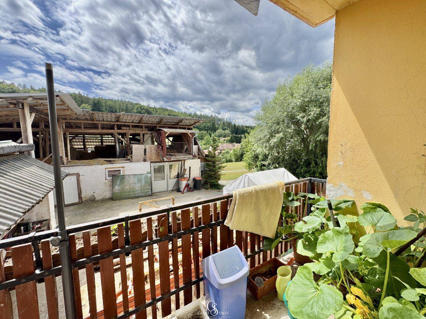 Balkon mit Pflanzen und Blick auf landwirtschaftliche Gebäude und die Umgebung.