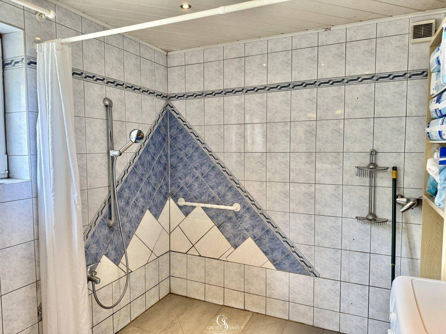 Duschbereich im Badezimmer mit blauen und weißen Fliesen in geometrischem Muster.
