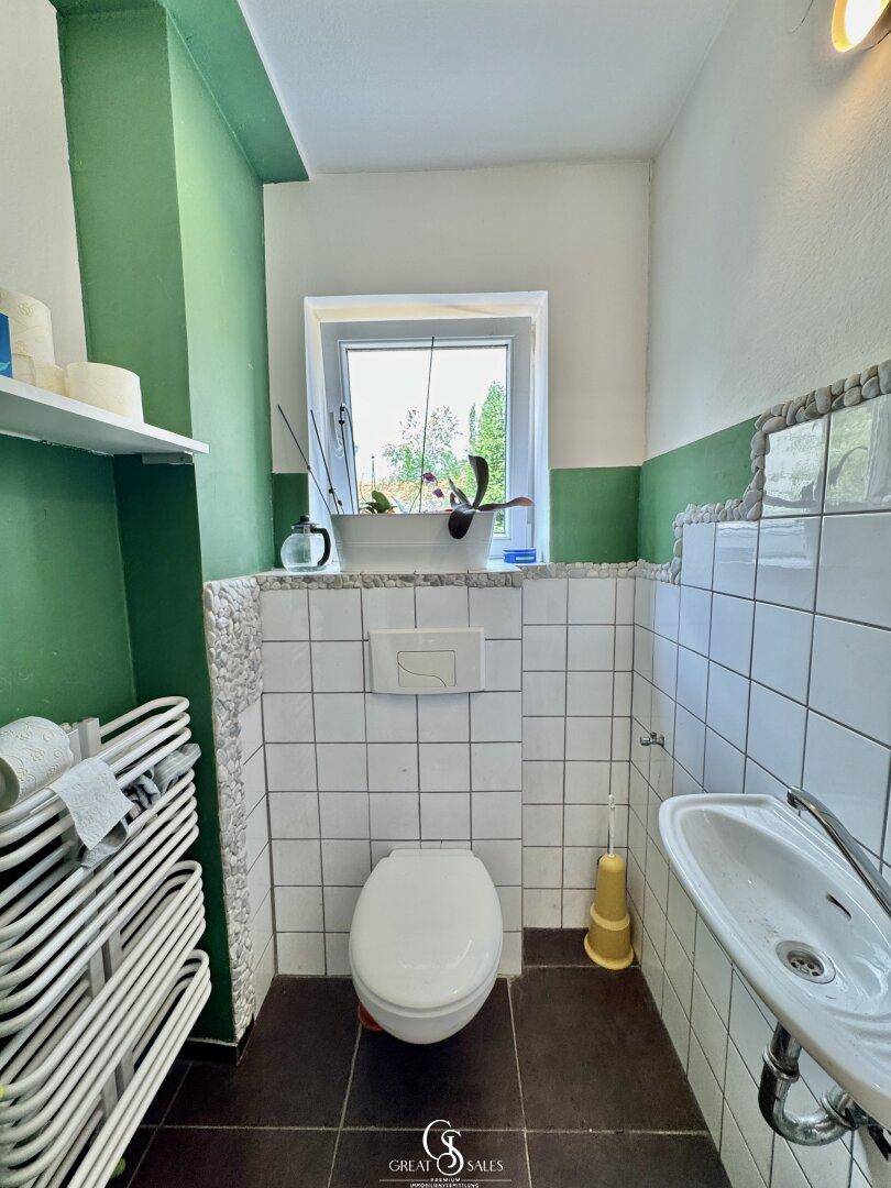 Kleines Gäste-WC mit Fenster, grünen Wänden und weiß-grünen Fliesen.