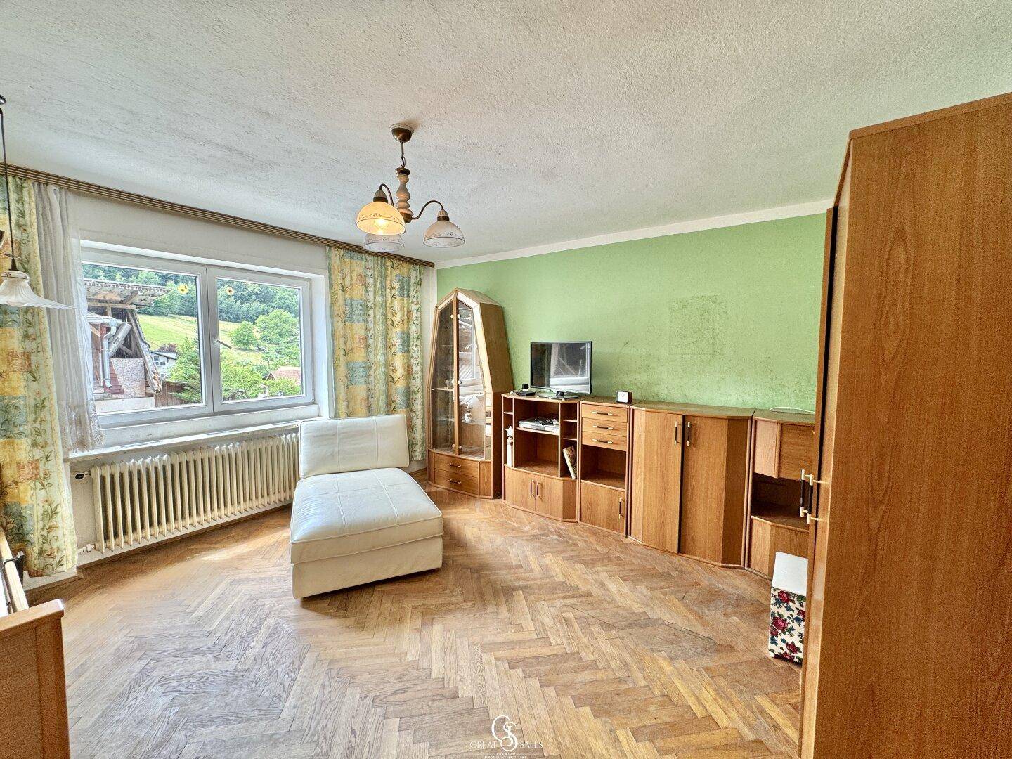 Wohnzimmer mit Fischgrätparkett, grüner Wand und Blick auf die Landschaft.
