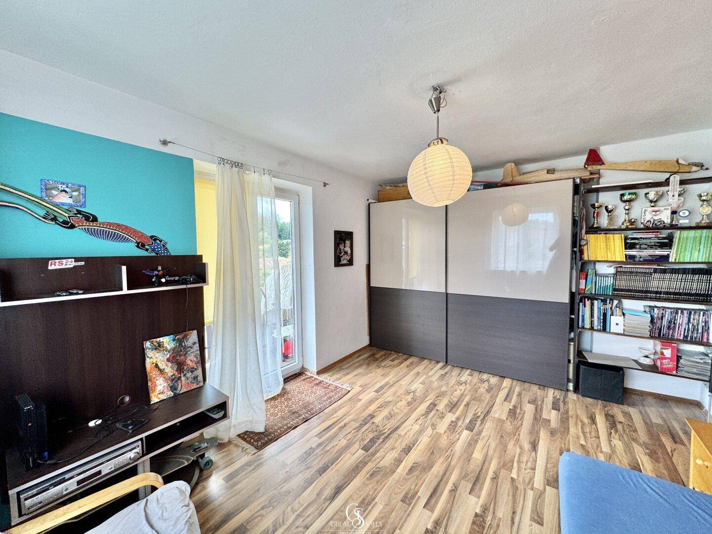 Schlafzimmer mit Laminatboden, Schiebetürenschrank und Zugang zum Balkon.