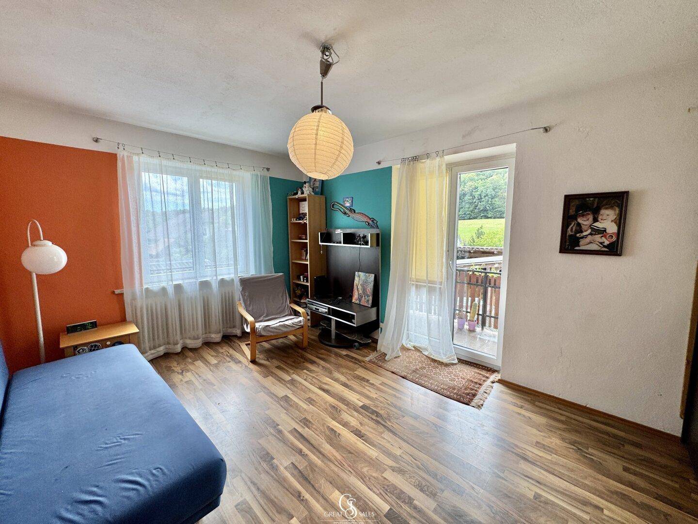 Wohnzimmer mit Laminatboden, farbigen Wänden und Zugang zu einem Balkon.