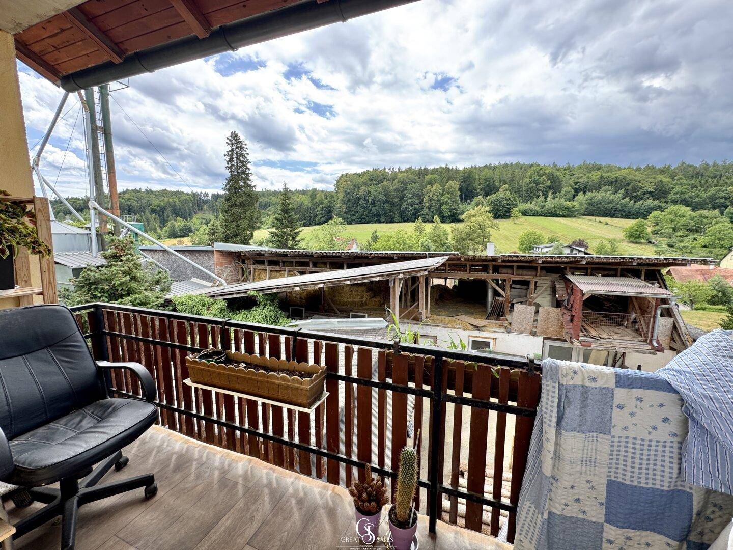 Balkon mit Holzboden und Blick auf die umliegende grüne Landschaft und Gebäude.