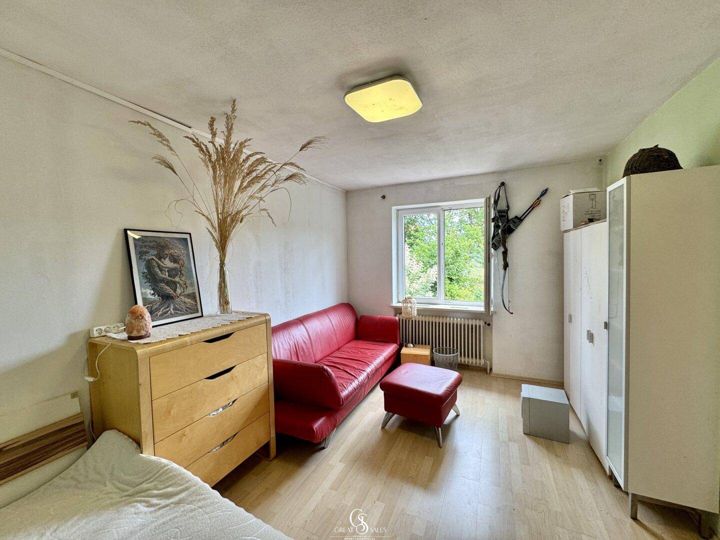 Schlafzimmer mit Laminatboden, rotem Sofa und Fenster mit Blick ins Grüne.