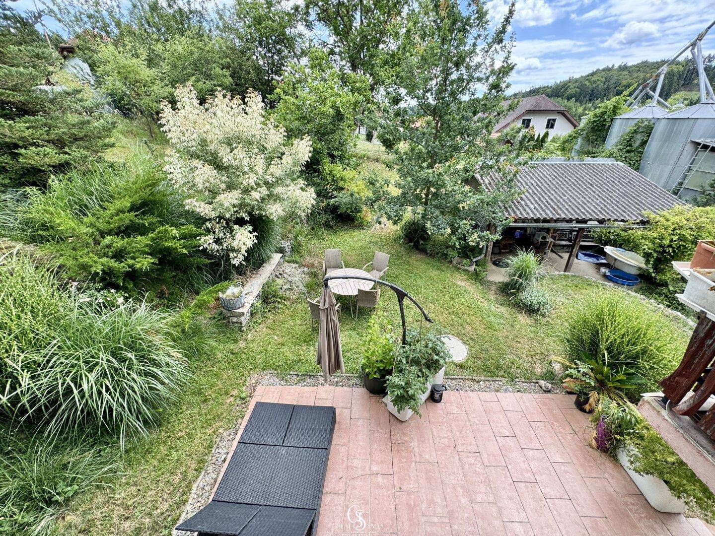 Gartenbereich mit Terrasse, Rasenfläche und Sitzgelegenheiten im Grünen.