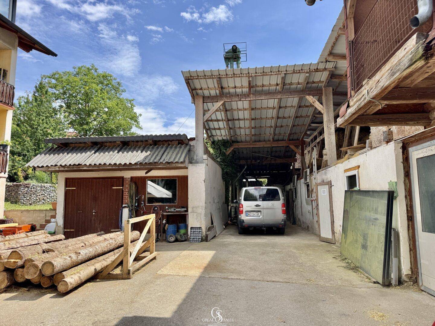 Außenansicht eines Bauernhofs mit Scheune, Garage und Holzstapel.