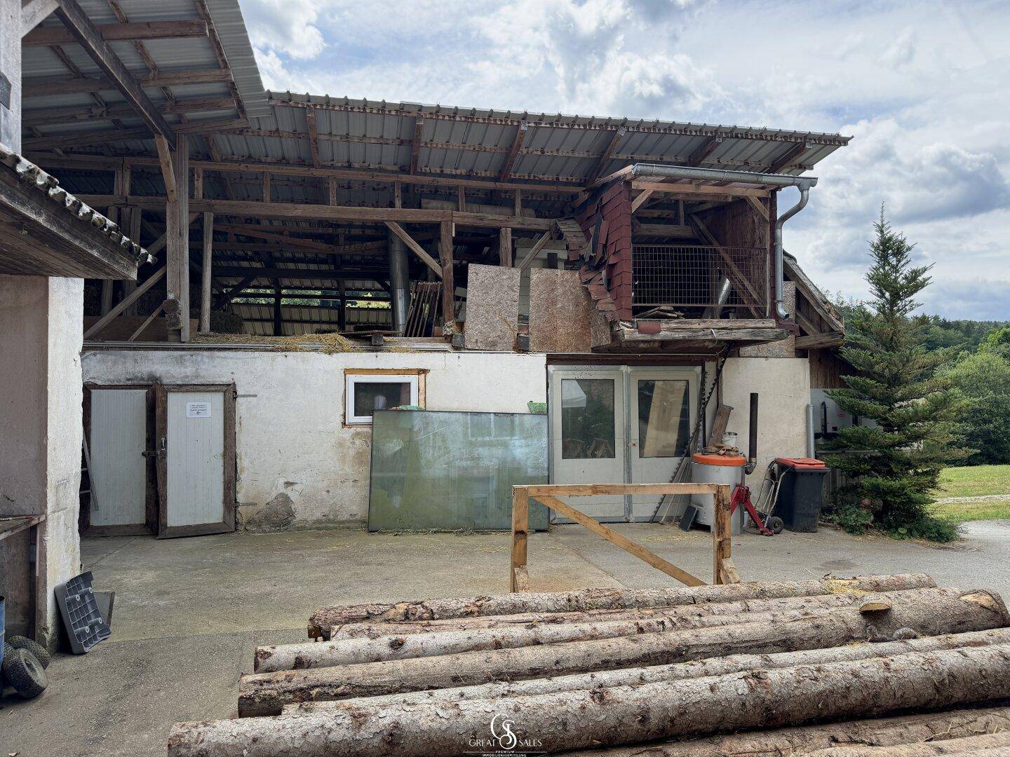 Rückansicht eines Bauernhofgebäudes mit Scheune und Holzstapel.