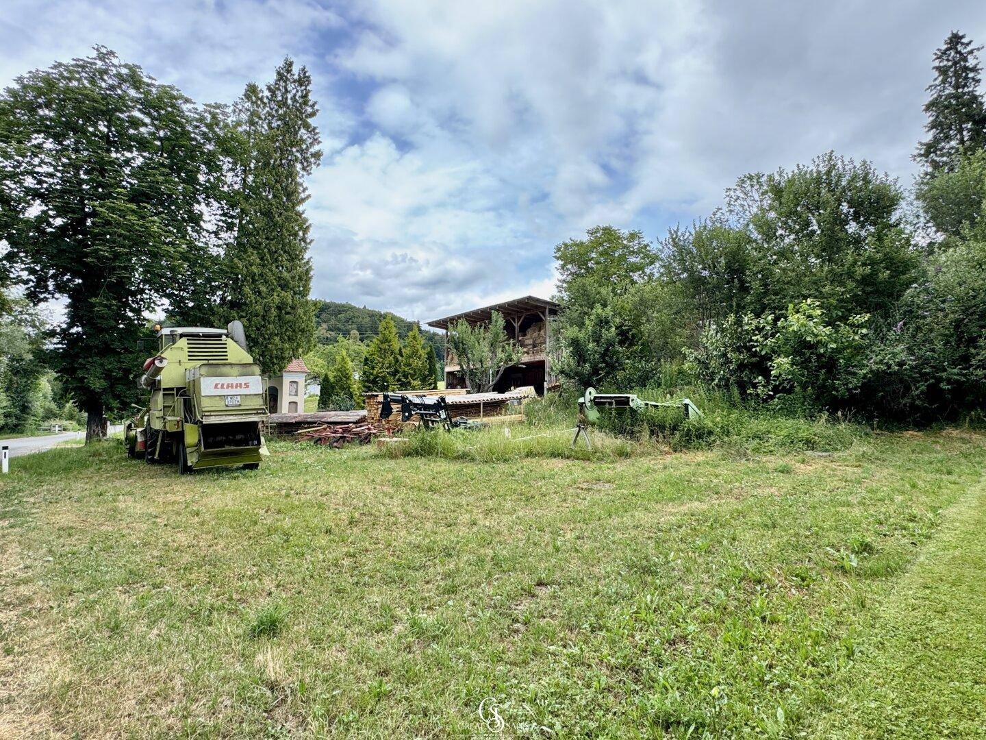 Weitläufiges Grundstück mit landwirtschaftlichen Geräten und Scheune im Hintergrund.