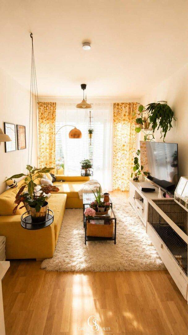 Gemütliches Wohnzimmer mit gelbem Ecksofa, weichem Teppich und vielen dekorativen Pflanzen.