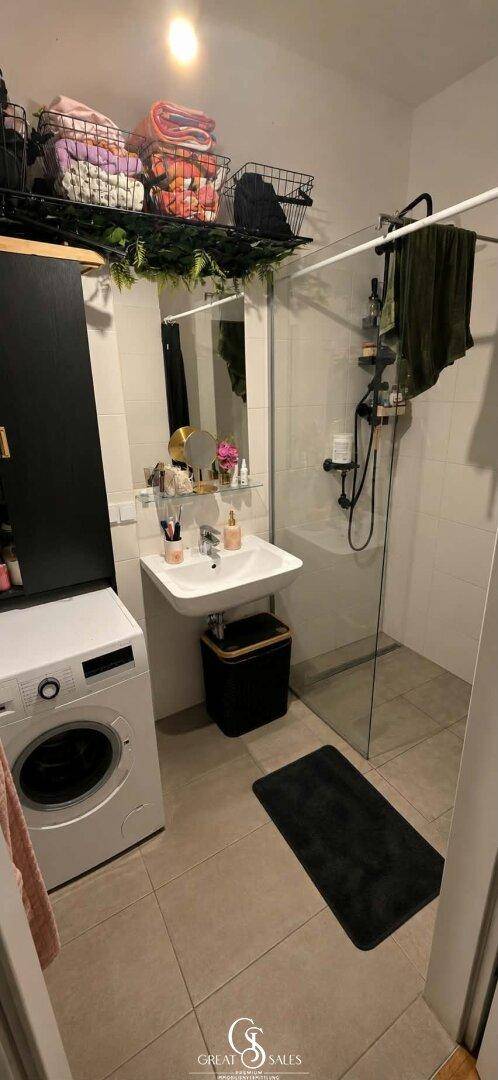 Modernes Badezimmer mit Dusche, Waschmaschine und praktischen Ablagemöglichkeiten für Handtücher.
