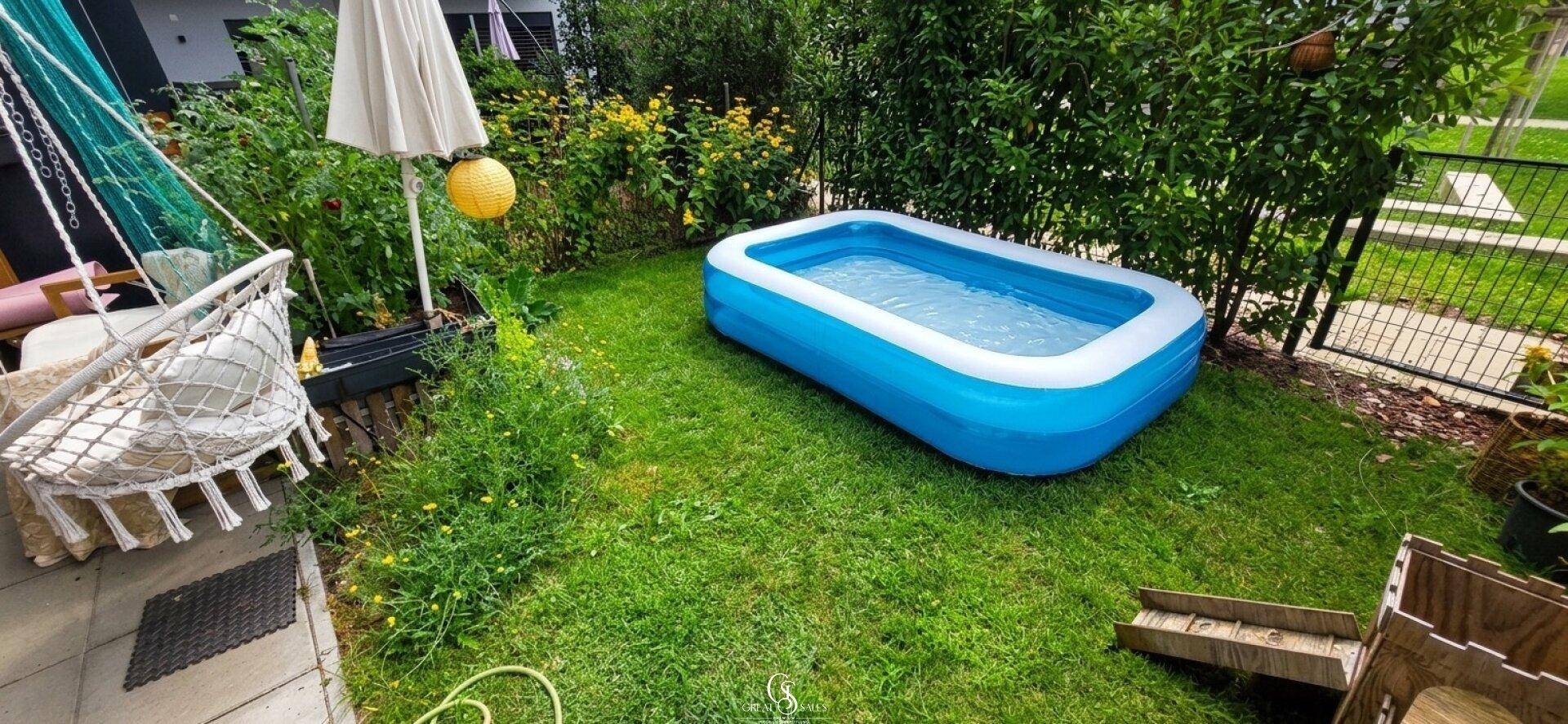 Grüner Garten mit Rasenfläche, aufblasbarem Pool und Hängesessel für sommerliche Entspannung.