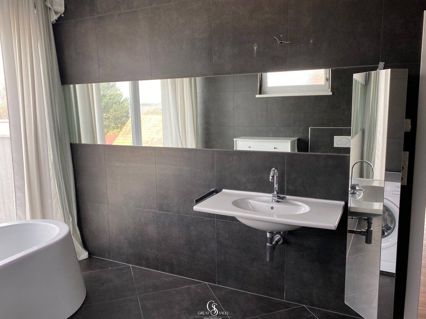 Modernes Badezimmer mit dunklen Fliesen, Einzelwaschbecken und großer Spiegelwand.