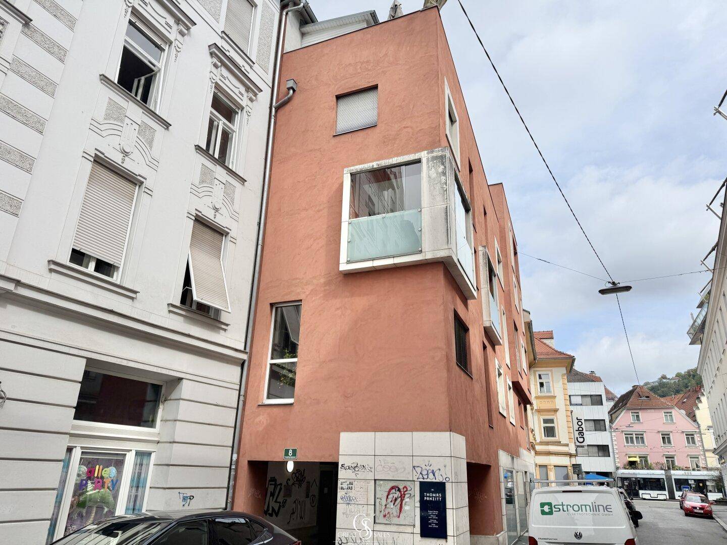 Moderne Gebäudefassade in Terrakotta-Farbe mit großen Fenstern und städtischer Umgebung.