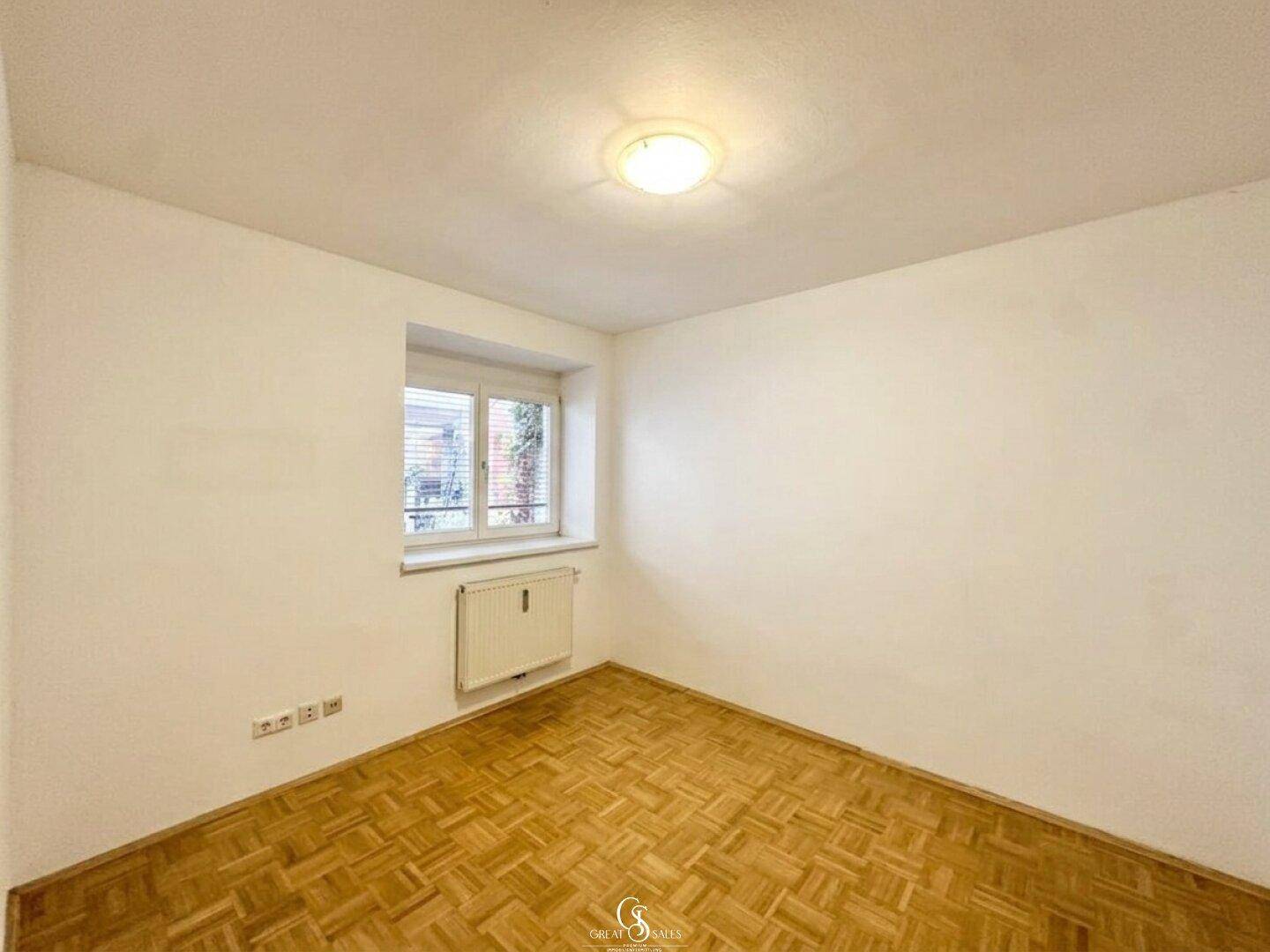 Geräumiges Schlafzimmer mit Parkettboden und einem Fenster mit Blick auf den Innenhof.