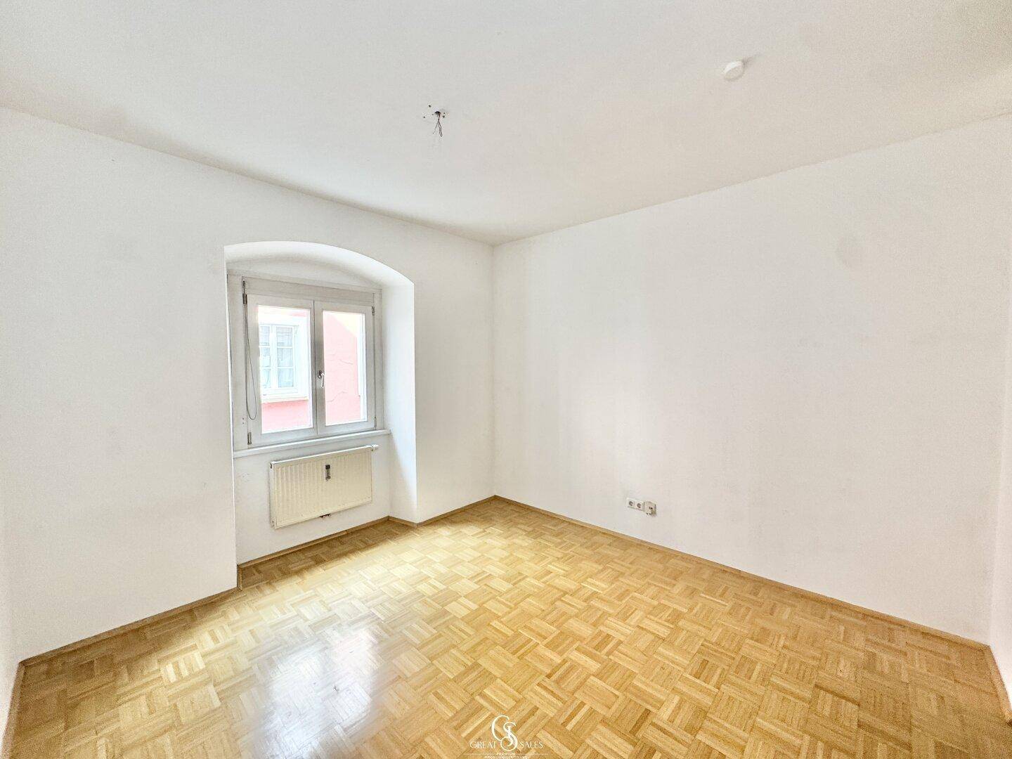Helles Schlafzimmer mit Parkettboden und einem Fenster, das viel Tageslicht hereinlässt.