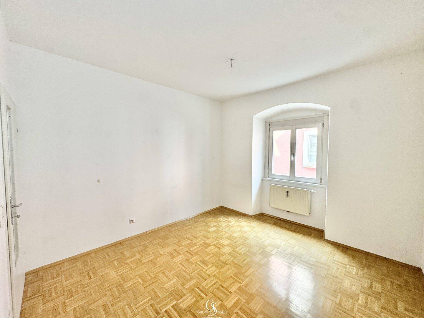 Geräumiges Schlafzimmer mit Parkettboden und einem Fenster mit Blick nach draußen.
