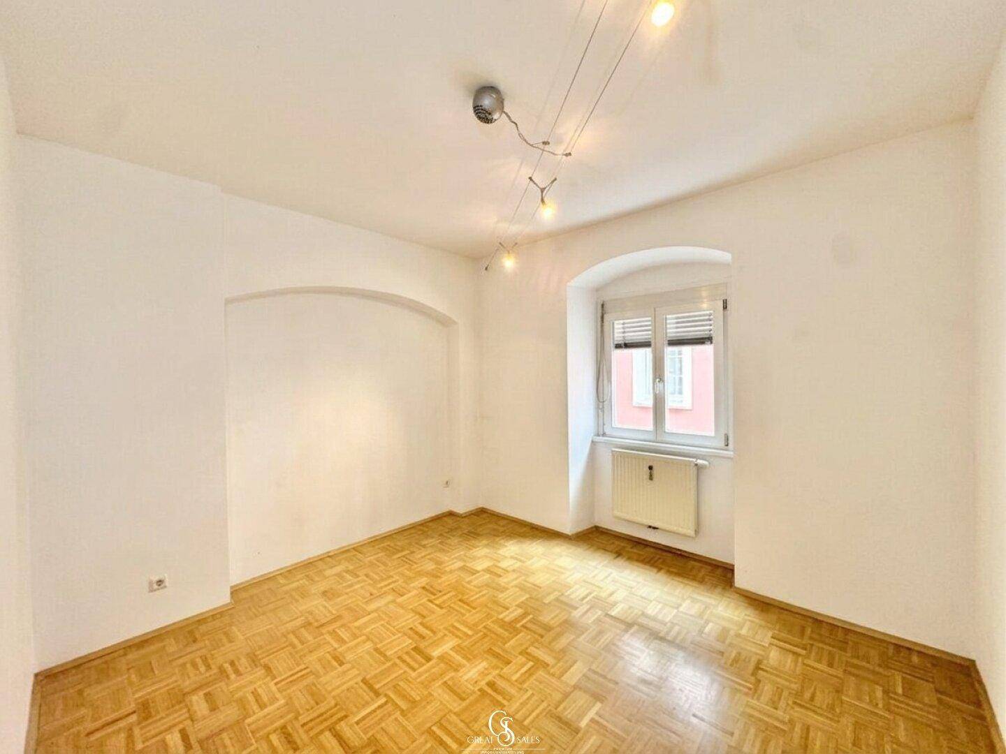 Schlafzimmer mit Parkettboden, Fenster und einer dekorativen Nische in der Wand.