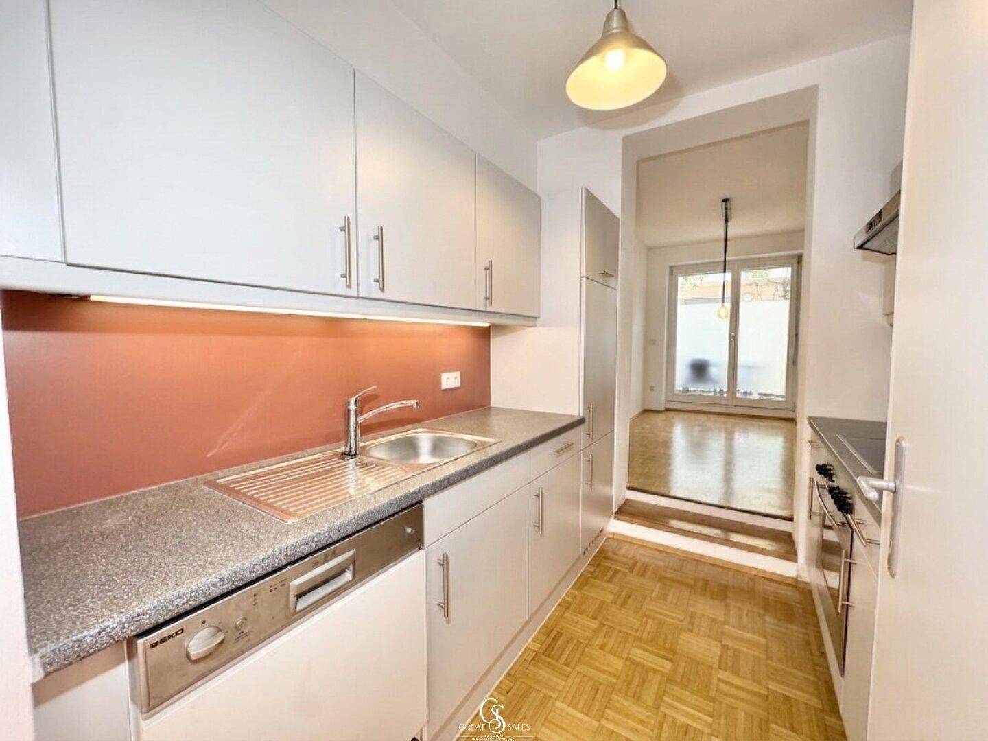 Helle Küche mit Spülmaschine, Spüle und Blick in den angrenzenden Wohnbereich.