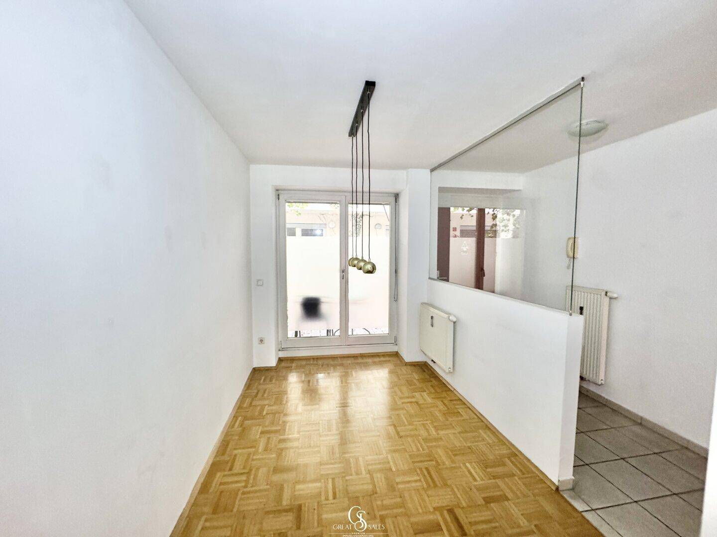 Geräumiger Wohnbereich mit Fischgrätparkett und viel Tageslicht durch die Terrassentür.