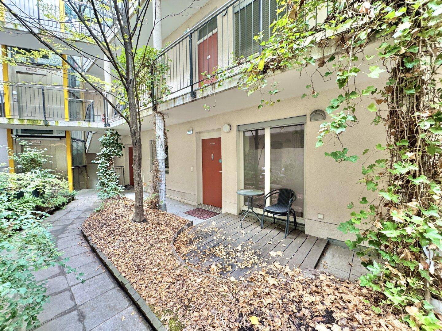 Kleiner, begrünter Terrassenbereich im Innenhof mit Sitzgelegenheit und viel Grün.
