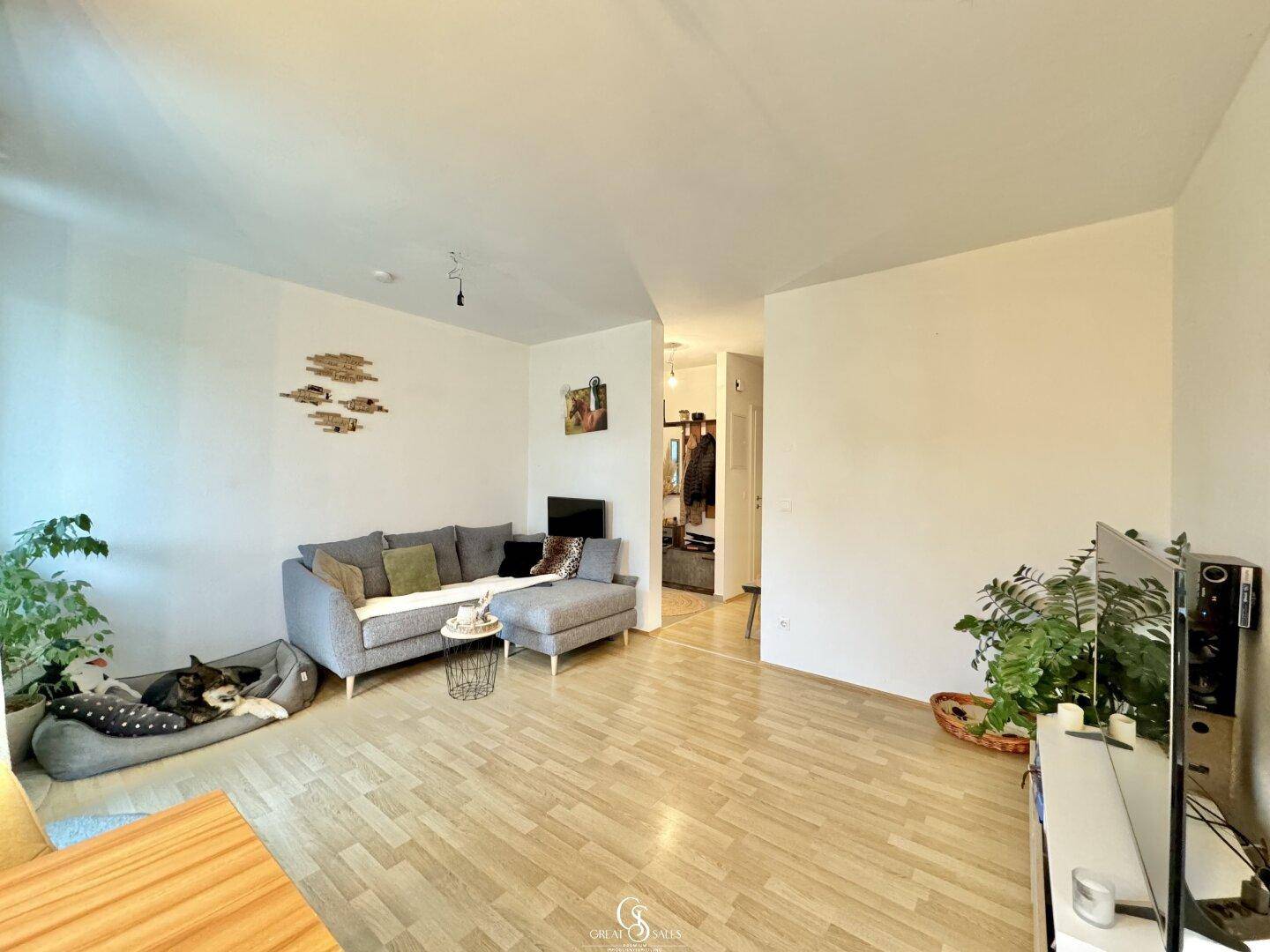 Gemütliches Wohnzimmer mit Sofa, Pflanzen und Holzboden, offen zum Flur, einladend gestaltet.