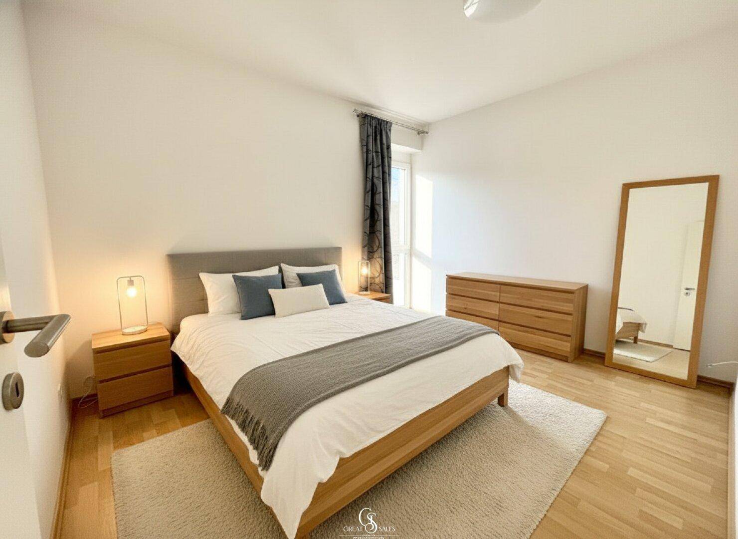 Gemütliches Schlafzimmer mit Doppelbett, Holzboden und großem Spiegel, hell und einladend.
